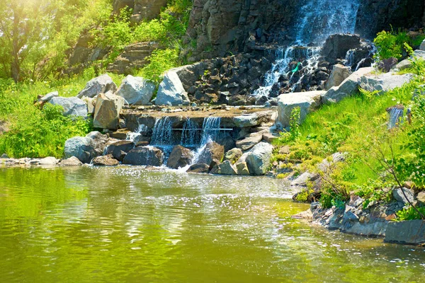 日光の下で美しい滝は、多くの美しい水の緑の森に囲まれたジェット. — ストック写真