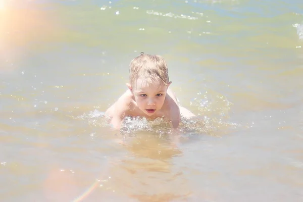 Petit garçon nageant dans la mer, courant et éclaboussant dans les vagues de pure . — Photo