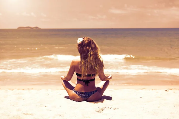 Uma menina jovem e bonita com cabelo ruivo, de biquíni. pratica ioga na areia branca e mar azul-turquesa . — Fotografia de Stock