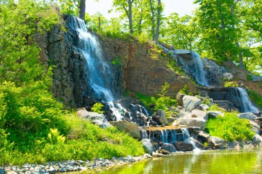 beautiful waterfall under sunlight, many beautiful water jets surrounded by green forests.  clipart