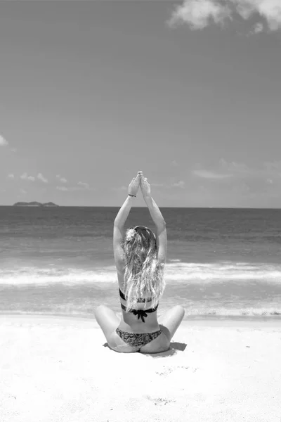 Uma menina jovem e bonita com cabelo ruivo, de biquíni. pratica ioga na areia branca e mar azul-turquesa . — Fotografia de Stock
