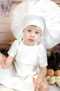 Küçük çocuk kek ve krep hazırlıyor. Bir şef çocuk hamuru gibi giyinmiş yemek hazırlar. 