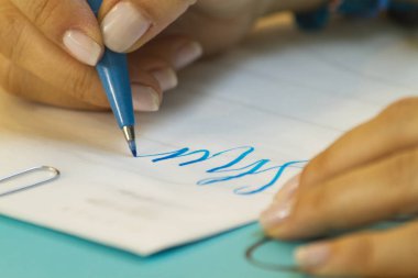 Mano aprendiendo harf en clase con lapicero azul y papel blanco