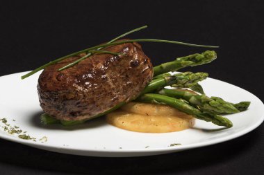 Carne con esparragos y pia en plato blanco y fondo negro