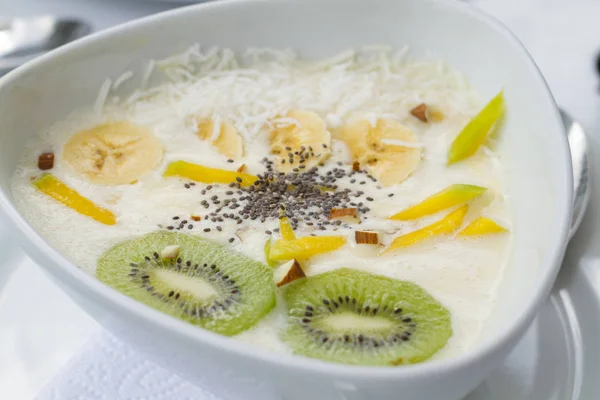 Yogurt con kiwi mango chia en plato de ceramica blanco con manteles blancos