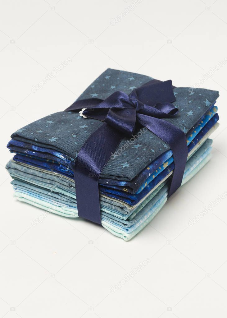 Pila de telas plegadas de colores azules con cinta de regalo desde arriba.