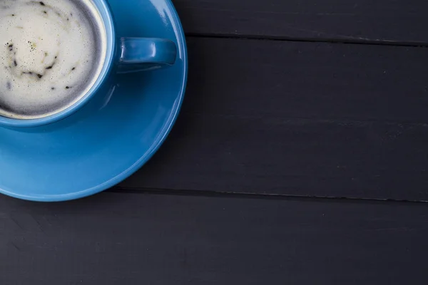 Cafe en taza azul con plato que le hace juego en fondo de madera negra en una esquina con espacio negativo para texto