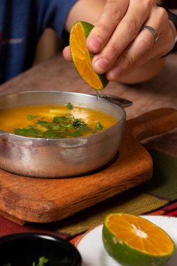 Mano de persona exprimiendo un limon en una sopa de papa con cilantro y perejil. Plato de comida Geleneksel Kolombiya