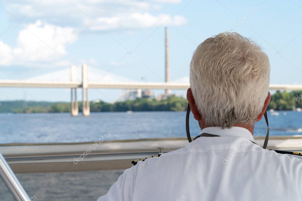 Over the shoulder POV view of a boat captain sailing down a river. Charting navigation path under bridge and past smoke stack factory on a clear summer day