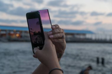 New York City, Circa 2019: Sosyal medya platformunda paylaşmak üzere güzel bir instagram resmi yakalamak için iPhone önünde gökyüzü renk efekti olan MpTV kameralı lens filtresi tutan eller