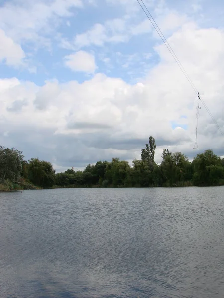 Landschap met bewolkte hemel, Cumulus wolken, groen bos en meer met reflecties in het water met wilgen en riet — Stockfoto