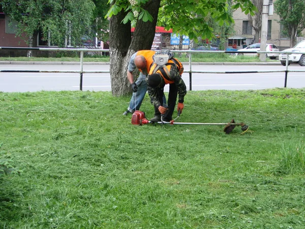 草刈りチームの作業中にガスハンドヘルドストリングトリマー機器を持つ男性労働者。ポルタヴァ, ウクライナ, 5月 12, 2019 — ストック写真