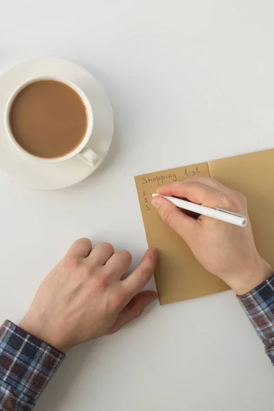 Üstten görünüm boş defter üzerinde yazma iş adamı. Gözlükler, kahve fincanı ile boş not defteri yazma adam el yüksek açılı görünüş. Erkek el notlar closeup.