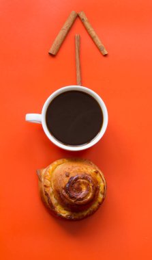 İsveçli. Tarçınlı çörek ve sade kahve fincanı, turuncu arka plan.