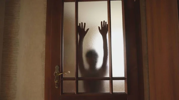 Behind the glass door is the silhouette of a girl. He touches the glass with his hands. A frightening picture. The ghost in the house. Halloween
