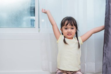 Güzel güzel çocuk kız evde iyi güneşli sabah sahiptir. Çocuk kız uykudan uyanır. Kızlar kollarını uzalar ve el kaldırırlar. İnsan sağlığı ve bebek yaşam tarzı kavramı.