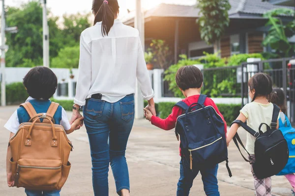 Group of mother and kids holding hands going to school with schoolbag. Mom bring children walk to school by bus together with satchel. Back to school and Education preschool. Parents son sister family