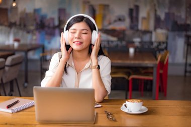 Rahatlatıcı ve kafede dizüstü bilgisayar ve kahve fincanı ile müzik dinlemek güzel Asyalı kadın. İnsanlar ve yaşam kavramı. Serbest mutlu işyeri tema. Üniversite ve kolej Tema.