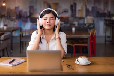 Rahatlatıcı ve kafede dizüstü bilgisayar ve kahve fincanı ile müzik dinlemek güzel Asyalı kadın. İnsanlar ve yaşam kavramı. Serbest mutlu işyeri tema. Üniversite ve kolej Tema.