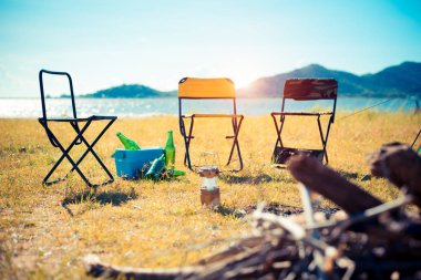 Çayır alan üç piknik sandalyeler. Ön plan ve arka planda dağ gölü kamp ateşi. Kamp ve kavram seyahat. Hiking ekipman Tema