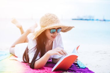 Güzellik Asyalı kadın tatil plaj var. Kanat şapka ve okuma kitabı renkli mat denize yakın giyen kız. Yaşam tarzı ve mutlu bir hayat kavramı. Seyahat ve tatil Tema.