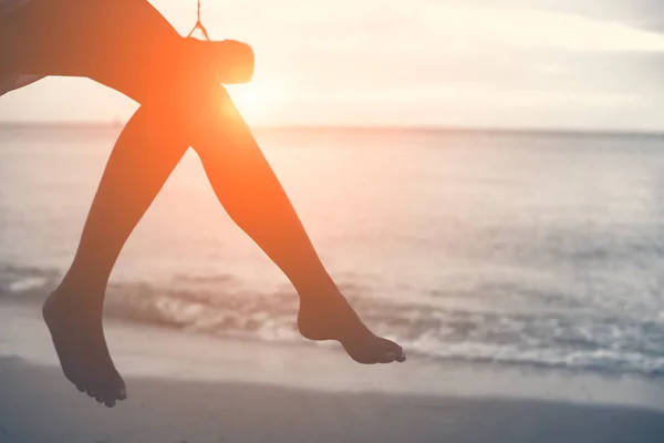 Woman legs at beach on wooden swing with sunset. Single woman concept. People and lifestyle concept. Lonely and sadness concept. Beach and sea theme. Finding soulmate theme. Copy space on right