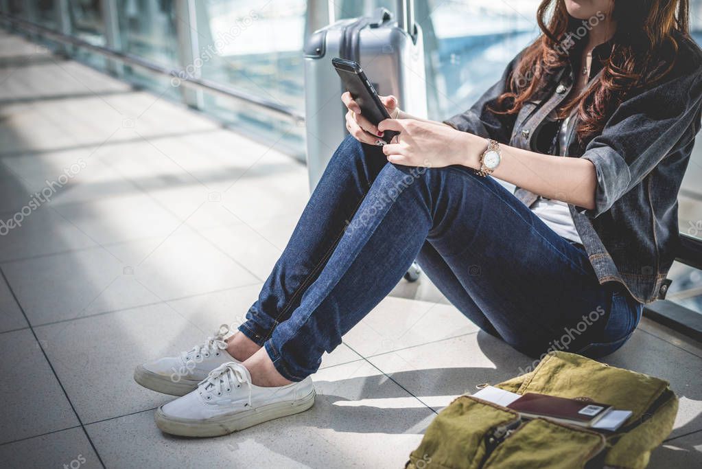 Close up of young woman with bag and suitcase luggage waiting for departure while sitting in airport lounge. Female traveler and tourist theme. High season and vacation concept. Relax and lifestyles