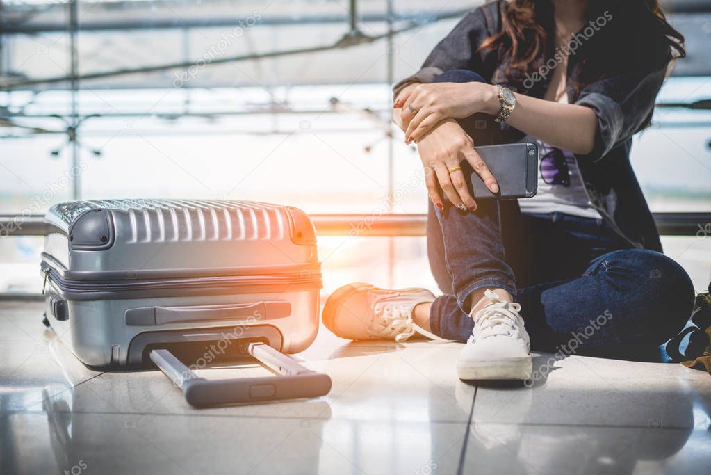 Close up of young woman with bag and suitcase luggage waiting for departure while sitting in airport lounge. Female traveler and tourist theme. High season and vacation concept. Relax and lifestyles