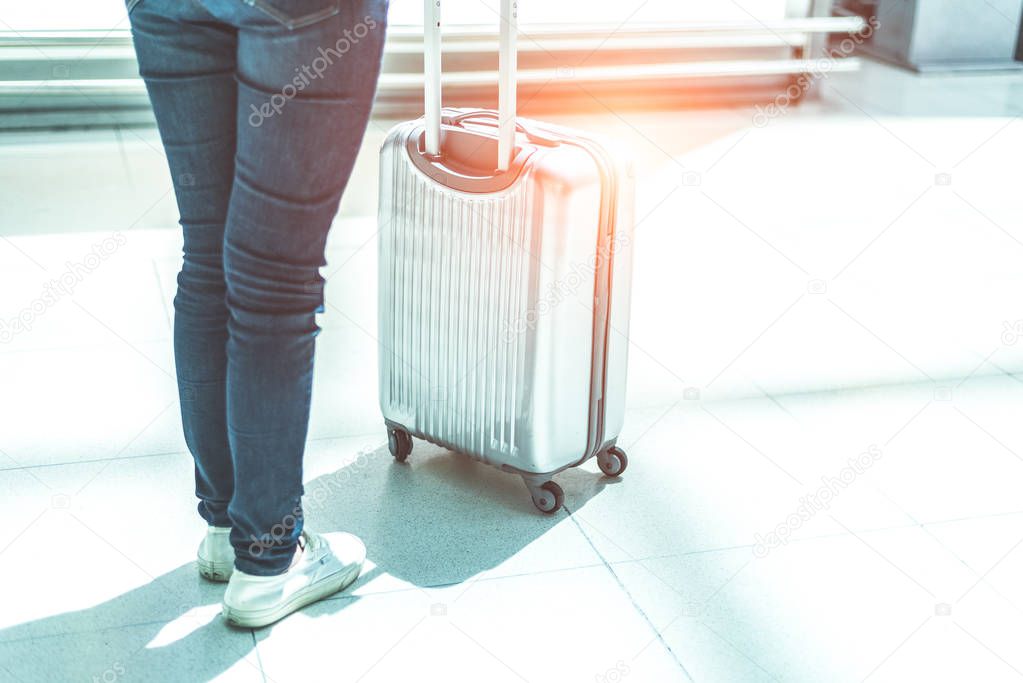 Close up woman and suitcase trolley luggage in airport. People and lifestyles concept. Travel and Business trip theme. Woman wearing jeans going on tour and traveling around the world by alone.