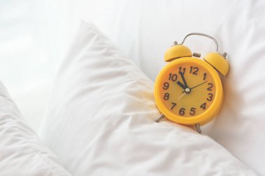 Beyaz yatak zemin üzerine sarı çalar saat. Seyahat ve tatil kavramı. Ev nesne aksesuarları Tema.