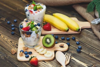 Sağlıklı bir Yunan Granola ve birçok meyve ile ahşap tabloda karışık meyveli yoğurtlu 