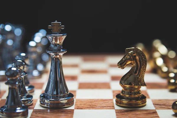 Strategy of strong leadership as king and weak leadership as horse facing each other in wooden chess board. Business marketing of competition trade partners tactics concept on black background