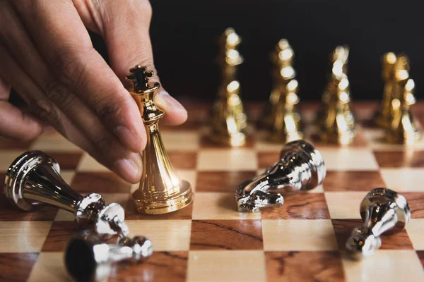 Hand of businessman moving golden chess figure for eliminating in battle competition with last successful ending game. Leadership strategy and management tactic concept. Wooden checkmate chessboard