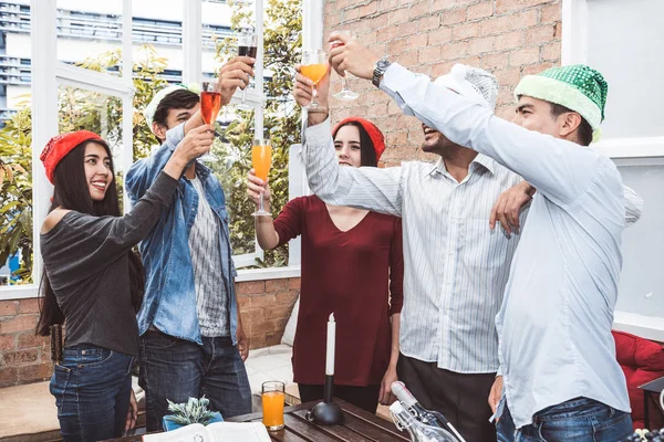 Outdoor Xmas party shot of young people toasting drinking glass at a rooftop terrace as forever friendship. Young friends hang out with alcohol drinking and juice. Christmas and New year party theme.