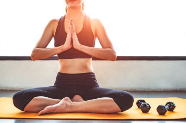 Yoga yaparken görünüm güzellik kadın önden ve elinizi kaldırın ya da fitness egzersiz eğitim spor merkezi hürmet ödemek. Mat ile spor ekipmanları ve egzersiz halter arka plan üzerinde oturan bir yaşam tarzı spor Bayan