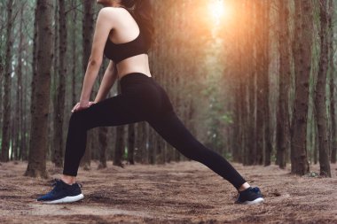 Yoga yaparken ve açık havada, ormandaki çalıştırmadan önce bacaklarını germe kadın daha düşük vücut yakın çekim. Spor ve doğa kavramı. Yaşam tarzı ve etkinlik kavramı. Çam ormanlar Tema.