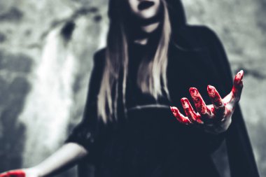Kanlı el gösterilen cadı. Siyah giysiler ve grunge duvar arka plan kaputa dişi şeytan melek. Cadılar Bayramı gün ve gizem kavramı. Sihirli Tema fantezi. Ölümden sonra yaşam ve ölüm kavramı.