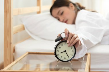 Asya genç güzellik kadın çalar saat sabah olmadan görünümlü saat geç ve tembel tatil çalışma için dönüm. Yatak odası ve yatak zaman kavramı. Gevşeme ve insanların yaşam tarzı yorgun işçi