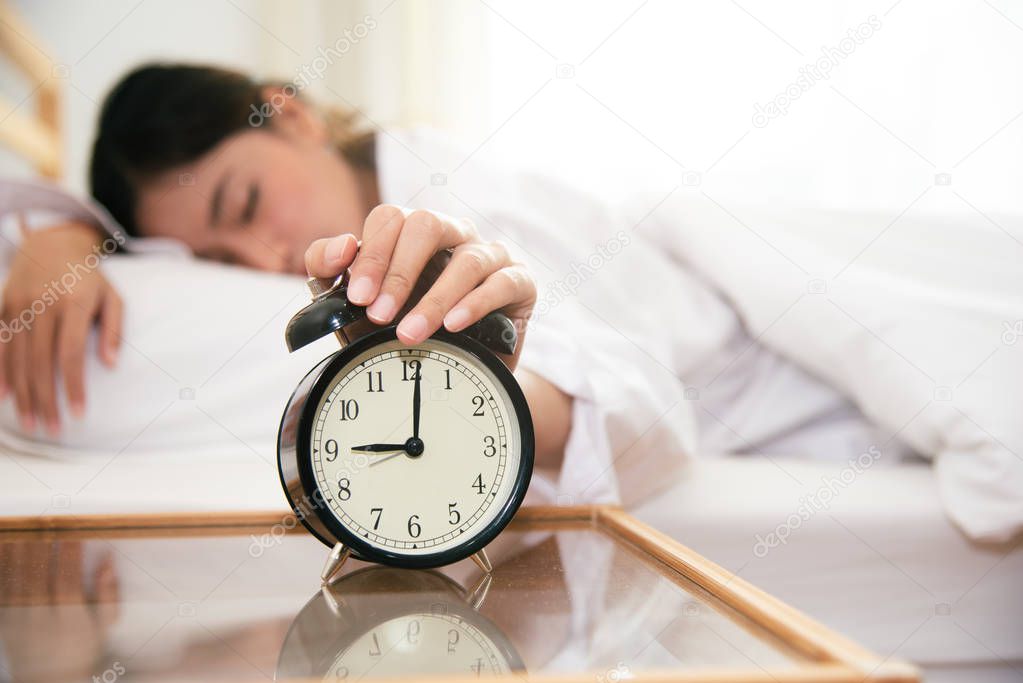 Asian young beauty woman turning off alarm clock in morning late without looking clock and lazy to working on in holiday. Bedroom and bed time concept. Relaxation and people lifestyles of tired worker