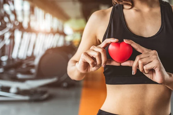 Mujer del deporte feliz sosteniendo el corazón rojo en gimnasio club de fitness. Médico —  Fotos de Stock