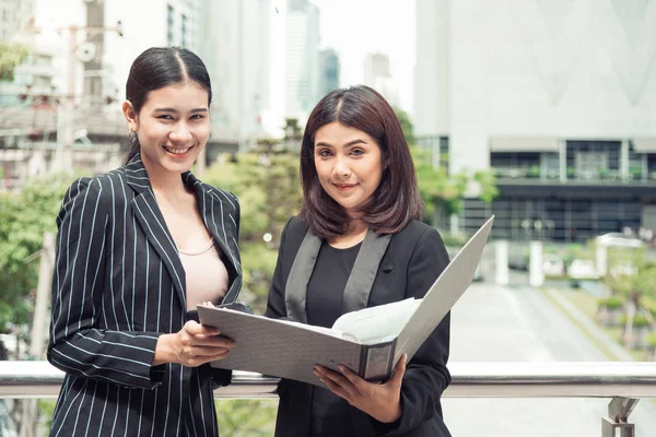 Two young Asian businesswomen looking into document file folder