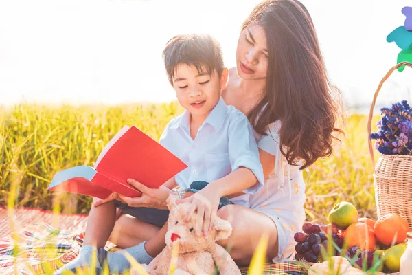 Little Asian boy and his mother reading books when doing picnic