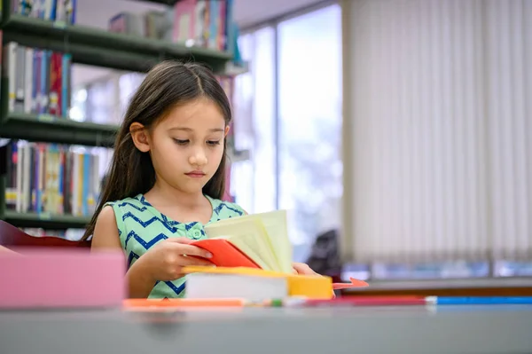 Aranyos kislány könyveket olvasott könyvtár figyelmesen az iskolában. — Stock Fotó