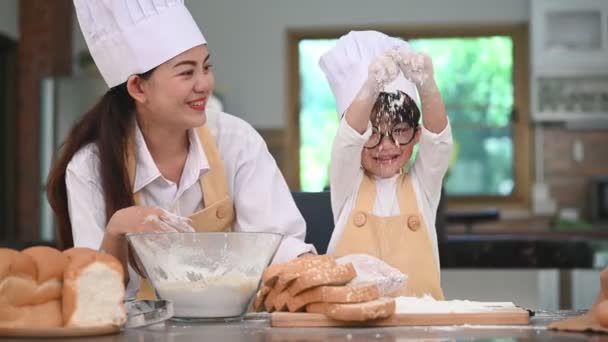かわいい小さなアジアの男の子と美しい母親は ベーカリーやケーキを焼く準備のためにテーブルの上に家庭用キッチンで生地の小麦粉をふるいます シェフとして小麦粉で遊ぶタイの子供たちは面白いです 幸福家族生活コンセプト — ストック動画