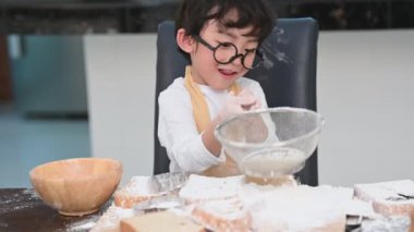 Sevimli küçük Asyalı çocuk fırın ve kek pişirme hazırlamak için ev mutfağında elerek elek colander ile hamur unu elemek. İnsanlar yaşam tarzları ve Eğitim. Şef komik olarak un ile oynayan Tay çocuklar