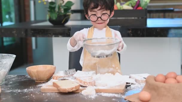 かわいいアジアの男の子は メガネ シェフの帽子とエプロンを再生し 家庭の台所でパン屋を焼くと面白いです 自家製の食べ物とパン 教育と学習の概念 肖像画と夢の仕事の職業 — ストック動画