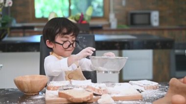 Sevimli küçük Asyalı çocuk fırın ve kek pişirme hazırlamak için ev mutfağında elerek elek colander ile hamur unu elemek. Taylandlı çocuklar şef komik olarak un ile oynuyor. İnsanlar çocuk oyun yavaş hareket