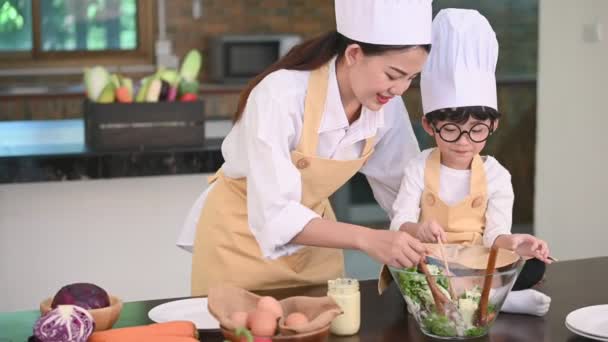 美しいアジアの女性と眼鏡をかけたかわいい男の子は 自宅で台所で調理する準備をします 人々のライフスタイルと家族 自家製の食べ物と食材のコンセプト ケト原性サラダを作る2人 — ストック動画
