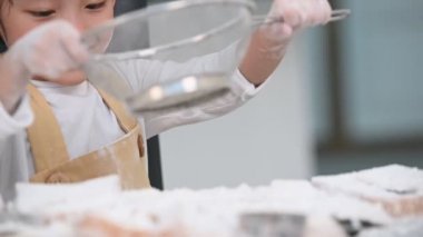 Sevimli küçük Asyalı çocuk fırın ve kek pişirme hazırlamak için ev mutfağında elerek elek colander ile hamur unu elemek Closeup. Taylandlı çocuklar şef komik olarak un ile oynuyor. İnsanlar yavaş çekim