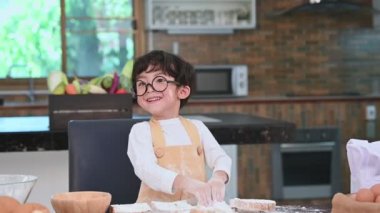 Gözlük ve önlük ile Sevimli küçük Asyalı çocuk şef komik olarak ev mutfağında oyun ve fırın pişirme. Ev yapımı yemekler ve ekmek. Eğitim ve öğrenme kavramı. Portre ve rüya iş meslek.